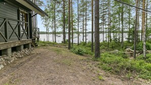 Een chalet met een grindpad dat leidt naar een steiger boven het water, omgeven door hoge bomen.