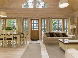 L’intérieur chaleureux d’un chalet comprend un coin repas, un canapé et de grandes fenêtres qui offrent une vue sur le paysage extérieur.