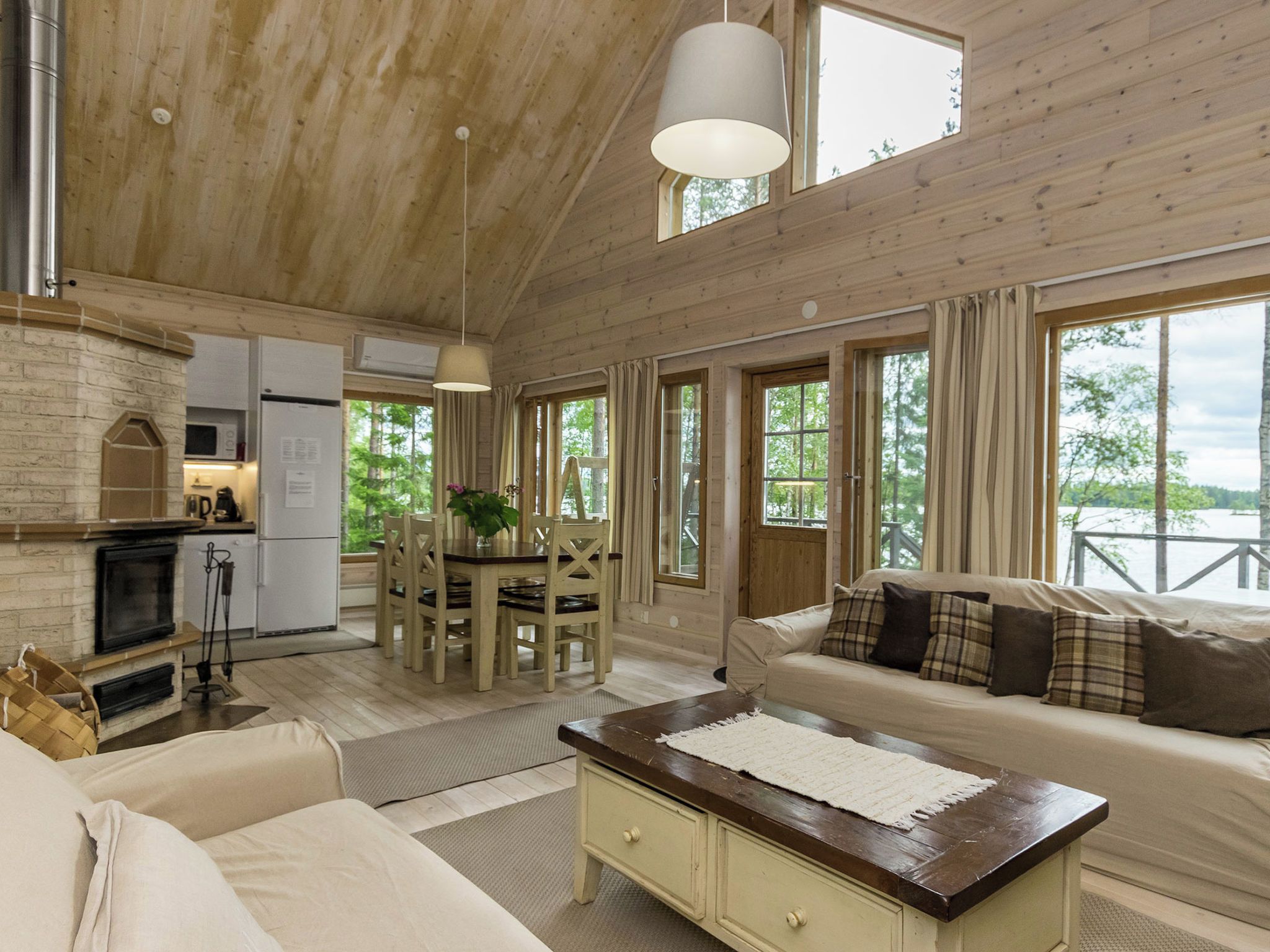A spacious living area with a fireplace, a sofa, a dining table with chairs, and large windows offering a view of the outdoors.