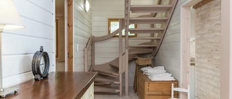 Un interior de madera con una escalera, un banco de madera y una pequeña mesa con un reloj.