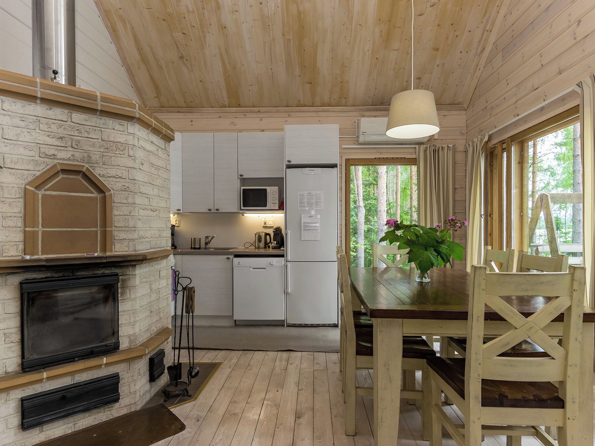 A cozy cabin interior with a fireplace, wooden dining table, and a kitchen area.