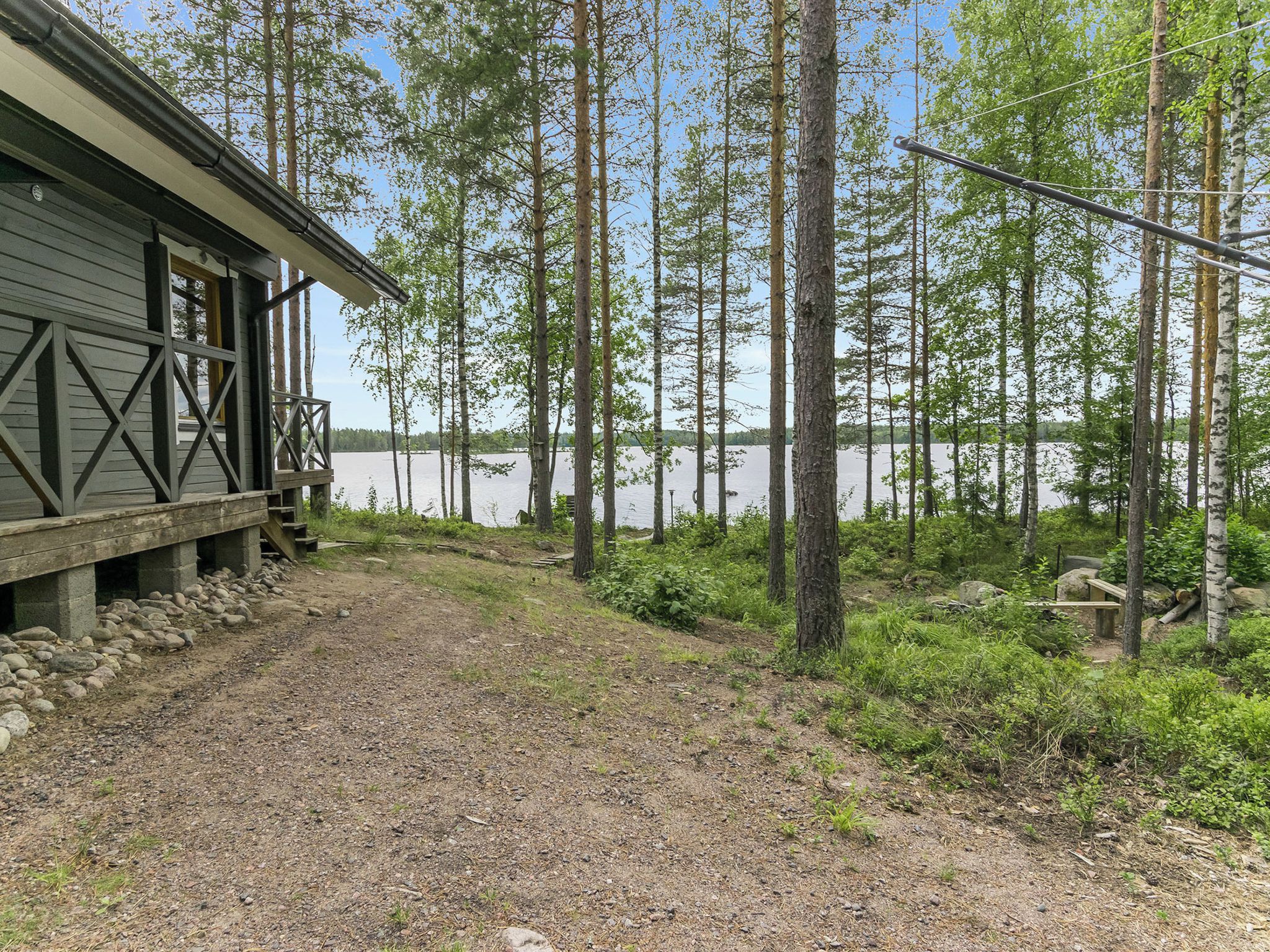 En stuga med en grusgång som leder till en brygga, omgiven av höga träd och en sjö eller ett annat vattendrag.