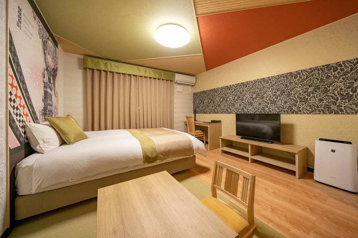 A hotel room with a bed, a TV, a desk, and a chair.