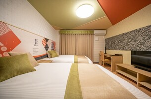 A hotel room with two beds, a desk, a chair, a television, and a wall with a floral pattern.