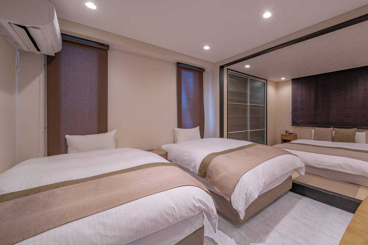 A hotel room with three beds, a sliding door, and a large window.