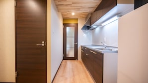 A narrow hallway with a wooden floor, a dark wooden door, and a kitchen area with a sink and cabinets. - Residence Hotel Takayama Station (Takayama)