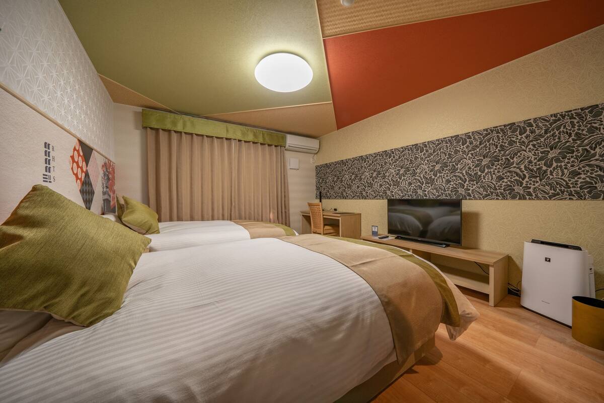 A hotel room with two beds, a television, a desk, and a refrigerator.