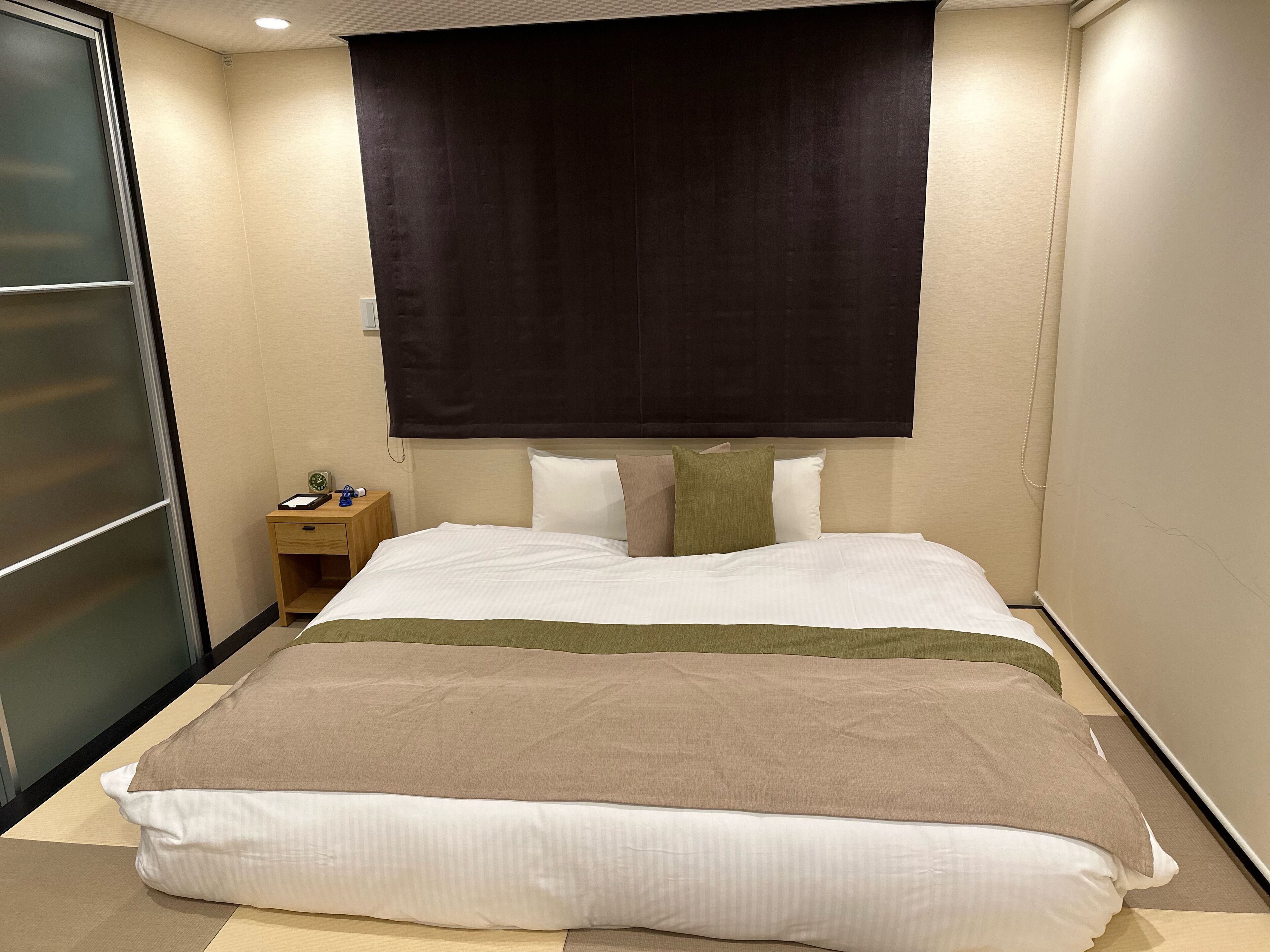 A hotel room with a large bed, a nightstand, a dark headboard, and a sliding door.