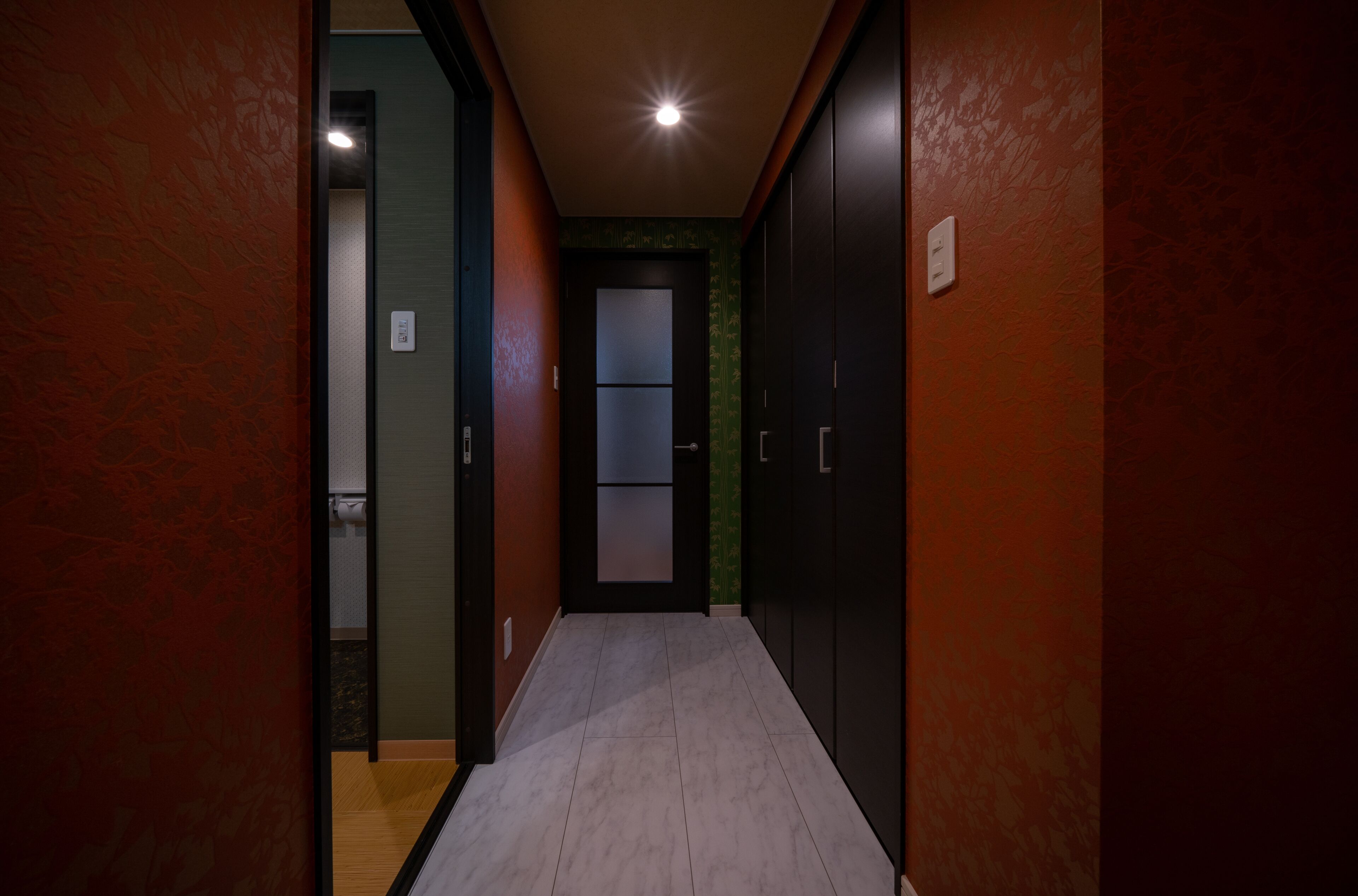 A narrow hallway with wooden flooring, red walls, and a door at the end.