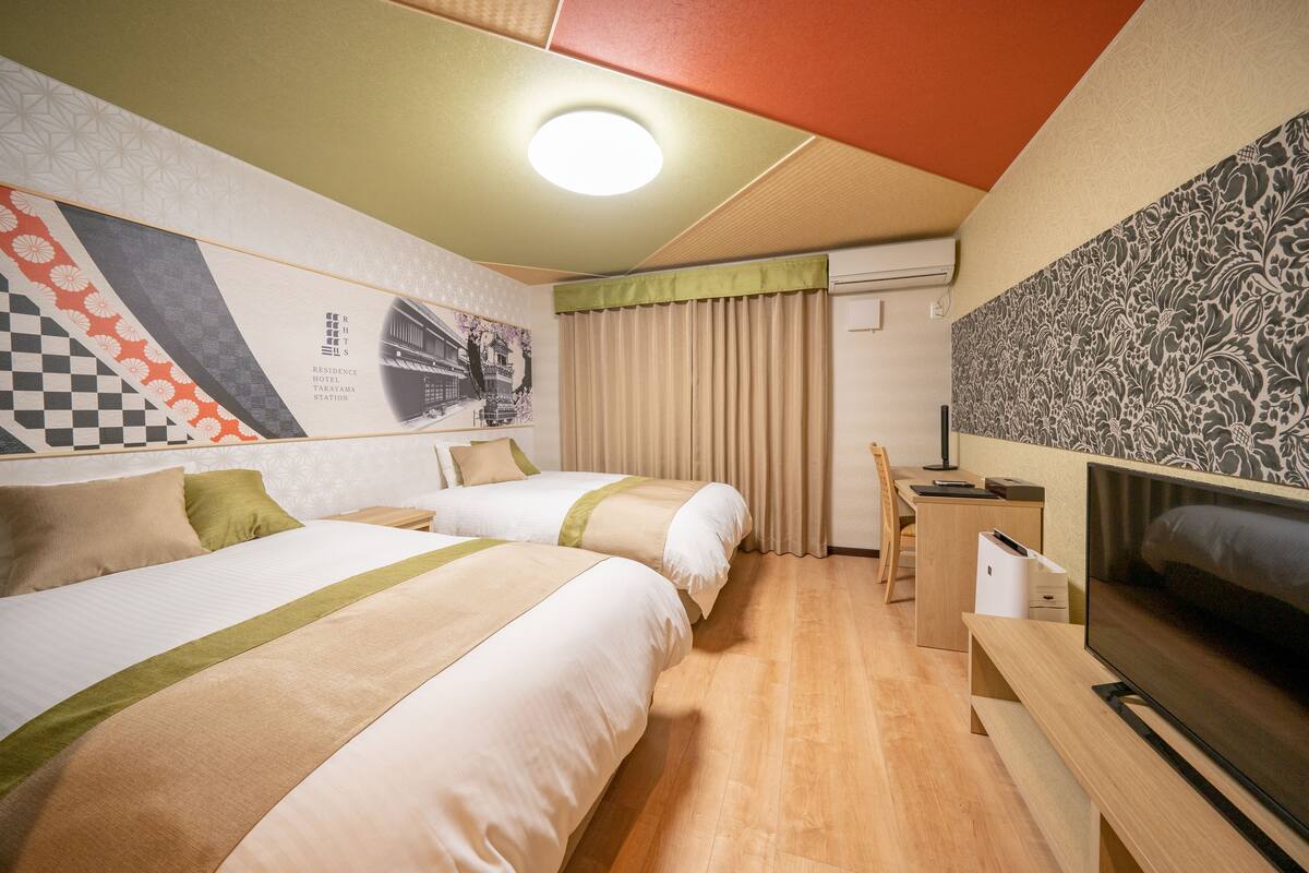 A hotel room with two beds, a desk, a TV, and a wall with a checkered pattern and a floral design.