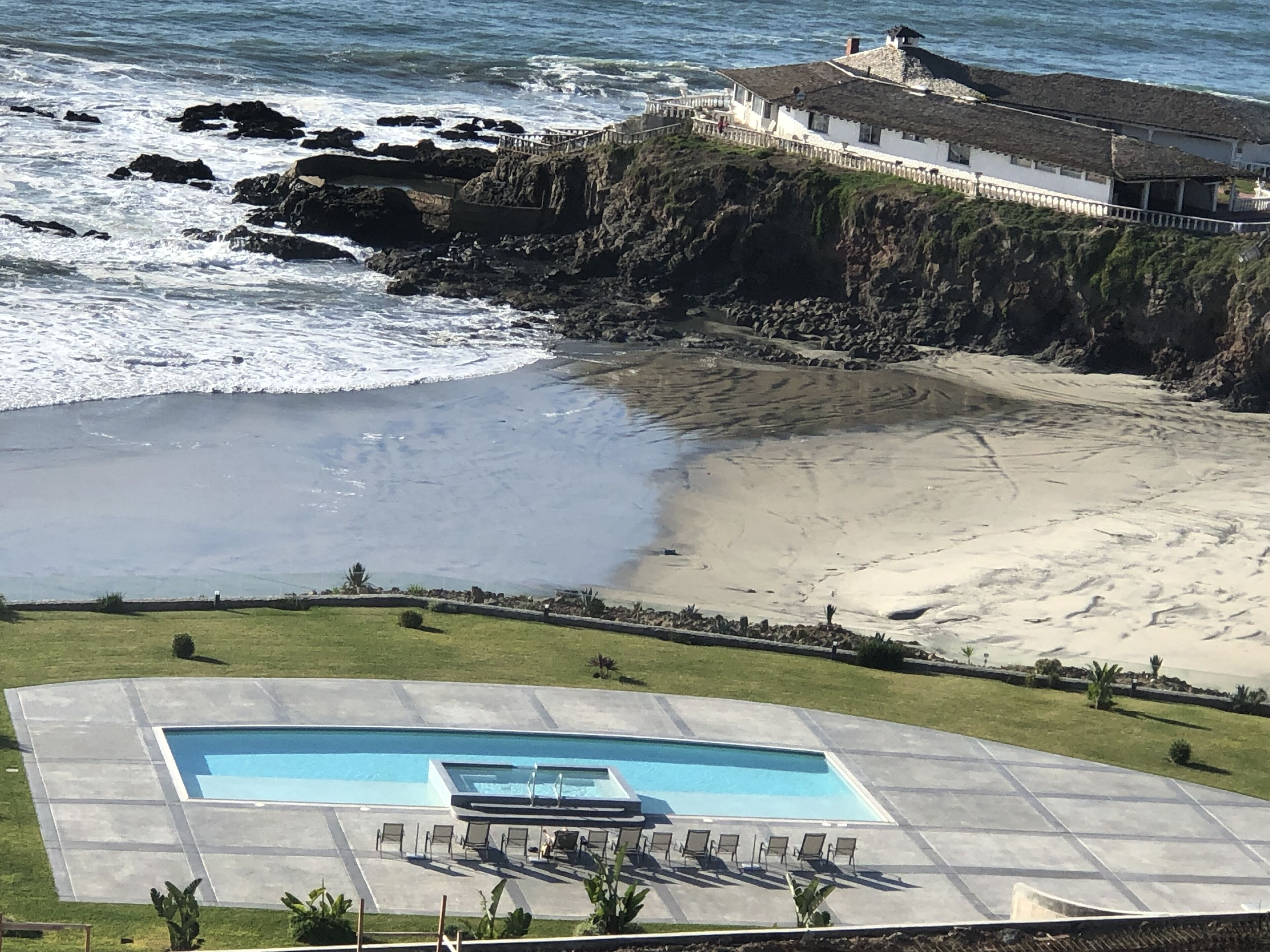 A coastal property with a swimming pool, beach access, and a large house overlooking the ocean.