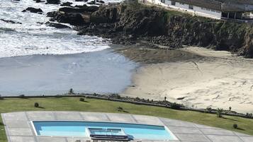 A coastal property with a swimming pool, beach access, and a large house overlooking the ocean.