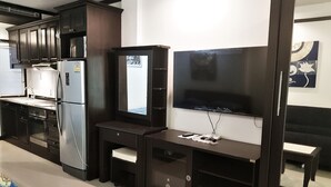 A modern kitchen with dark cabinetry, a stainless steel refrigerator, a built-in oven, and a flat-screen TV mounted on the wall. - Large Studio Baan Suan Lalana (Pattaya)