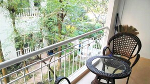 A balcony with wicker chairs and a glass table, overlooking a garden with trees and a pathway. - Large Studio Baan Suan Lalana (Pattaya)