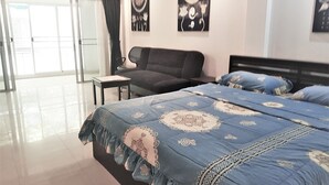 A hotel room with a large bed, a sofa, a small table, and a view through a large window. - Large Studio Baan Suan Lalana (Pattaya)