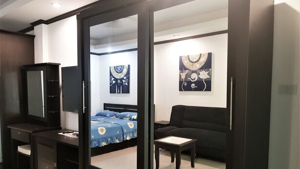A bedroom with a bed, a black sofa, a small table, a dresser, and a mirror. - Large Studio Baan Suan Lalana (Pattaya)