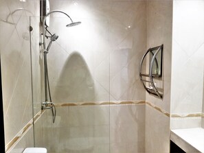 A bathroom with a glass-enclosed shower, a wall-mounted mirror, and a tiled floor. - Large Studio Baan Suan Lalana (Pattaya)
