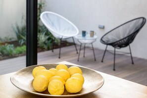 A table with a plate of lemons, a white chair, and a black chair in a modern outdoor setting.