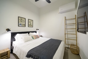 A neatly arranged bedroom with a bed, bedside lamps, a wall-mounted air conditioner, and a wooden ladder.