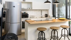 A modern kitchen with a central island, bar stools, a refrigerator, and a microwave. - Garden 1 Bedroom Apartment (Tel Aviv)