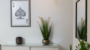 A framed playing card, a vase with a plant, and a mirror on a glass-top cabinet. - Garden 1 Bedroom Apartment (Tel Aviv)