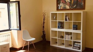 Een kamer met een witte boekenkast, een witte stoel en een schilderij aan de muur.