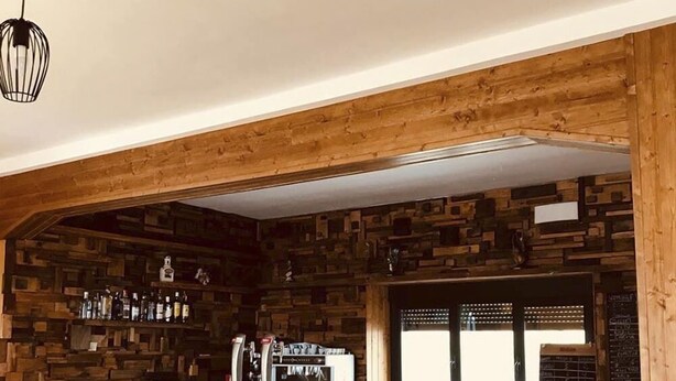 Een bar met een stenen muur, houten plafond en barstoelen met 'm'-logo's.