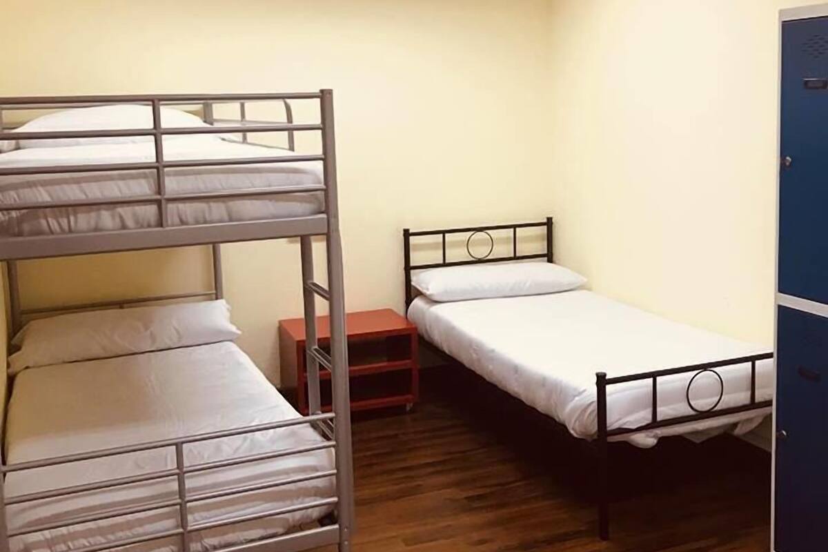 Een studentenkamer met stapelbedden en een enkel bed, houten vloeren en een blauwe kast.