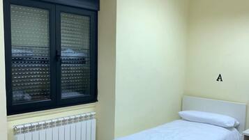 Een slaapkamer met een bed, een raam met zonwering, een radiator en een letter 'A' op de muur.