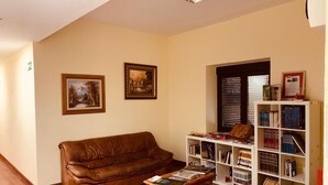 Een woonkamer met een bruine leren bank, een houten salontafel met tijdschriften, een witte boekenkast vol boeken en twee ingelijste foto's aan de muur.