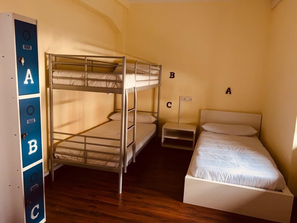 Une chambre de dortoir avec des lits superposés étiquetés A, B et C, une petite table de chevet et un lit simple.