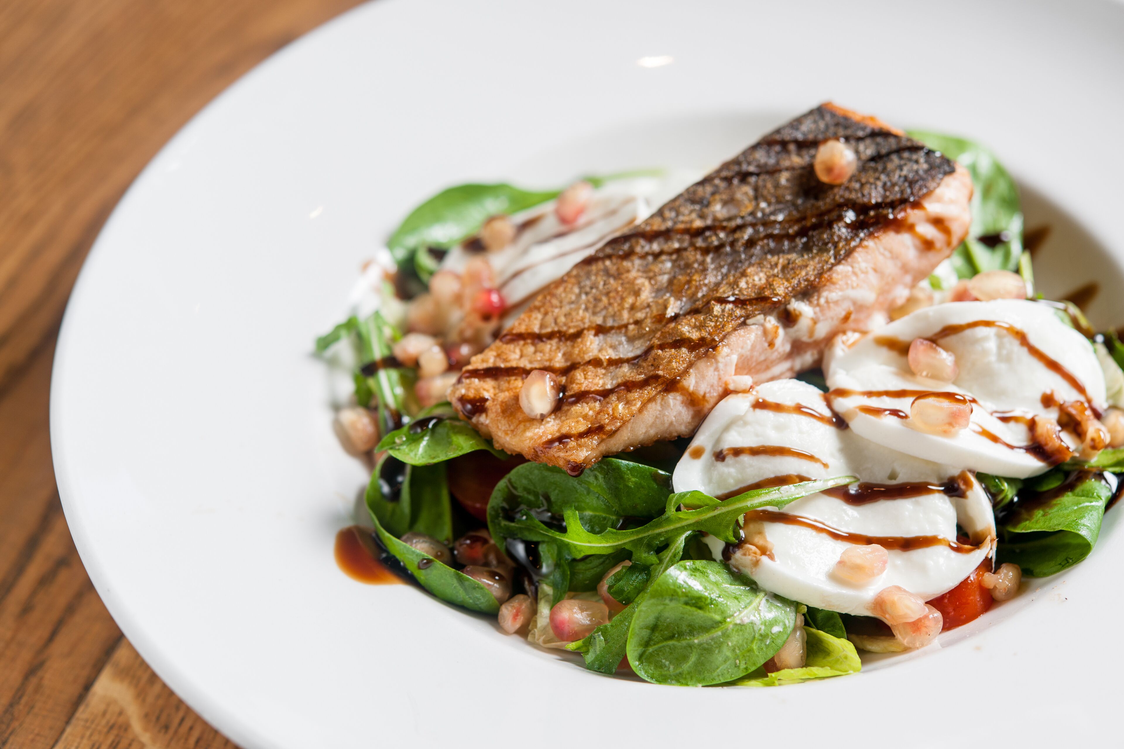 Um prato com peixe grelhado, legumes frescos e bolinhas de mussarela.