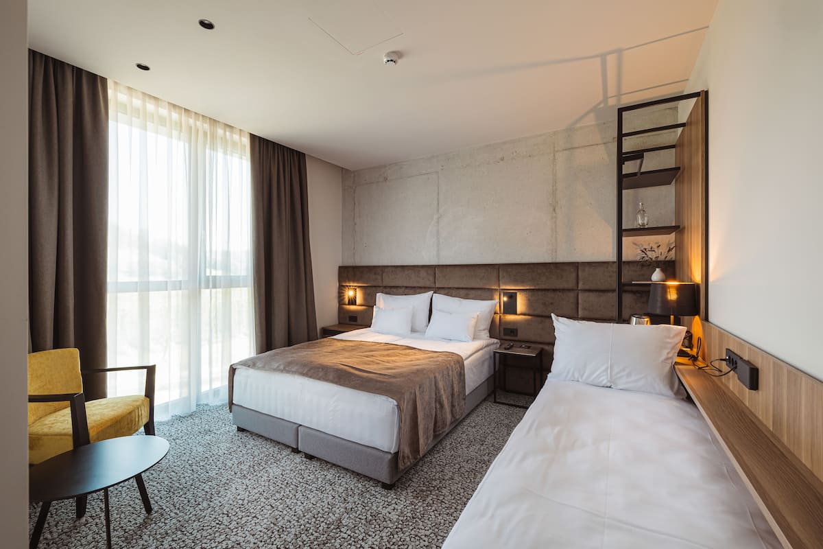 A hotel room with a large bed, a smaller bed, a chair, a desk, and a shelf with decorative items.