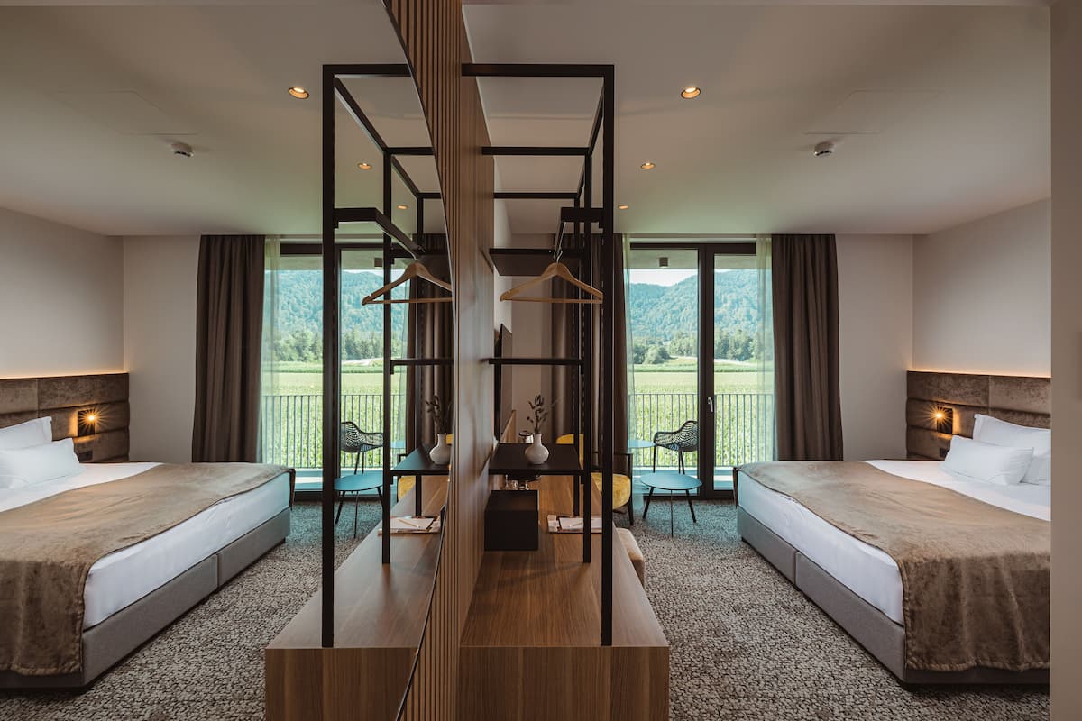 A hotel room with two beds, a central wooden structure, and a view of the outdoors.