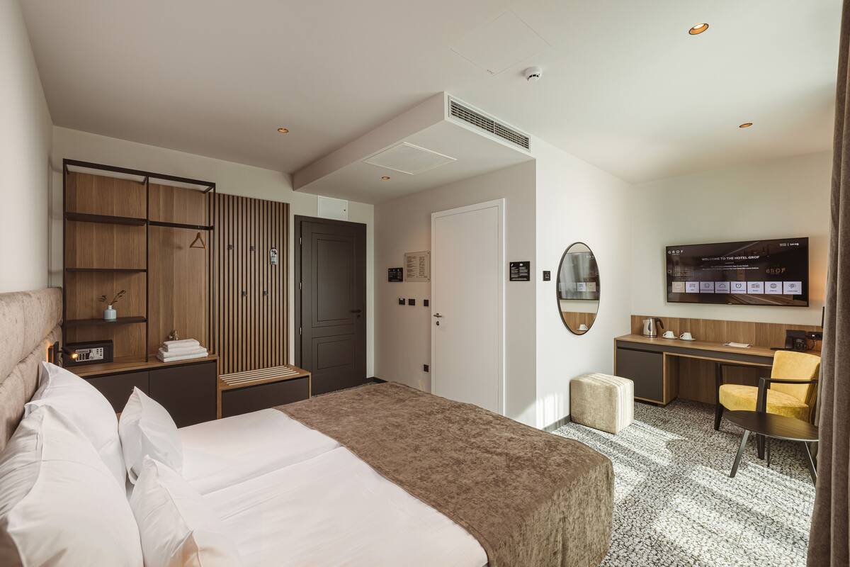 A hotel room with a bed, a desk, a chair, a wardrobe, and a television.