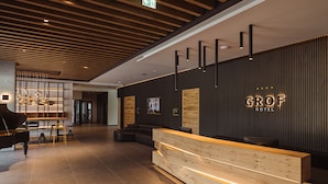 A modern hotel reception area with a wooden reception desk, black walls with vertical lines, and a black sofa. - Hotel Grof (Vransko)