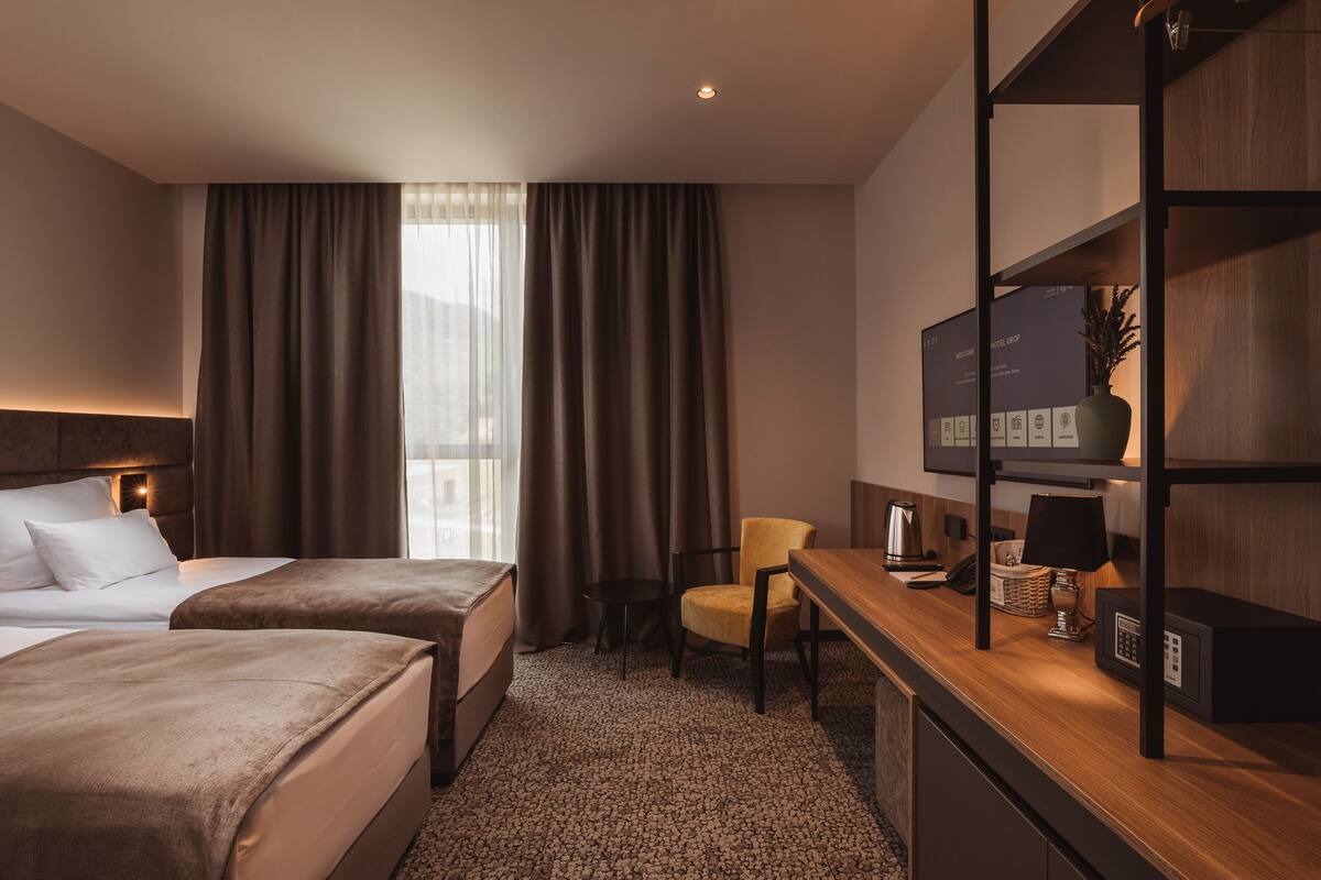 A hotel room with two beds, a desk, a chair, a television, and a coffee maker.