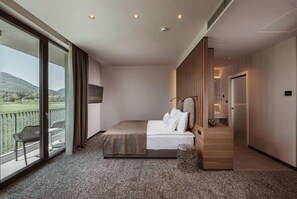 A hotel room with a large bed, a view of the outdoors, a balcony with a chair, and a wooden panel wall. - Hotel Grof (Vransko)