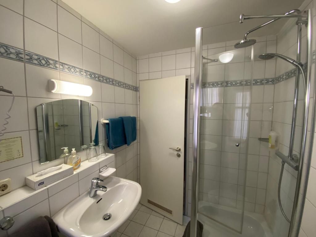 Un baño con lavamanos blanco, espejo y ducha con cerramiento de vidrio.