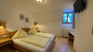 A bedroom with a wooden bed, bedside lamps, a flat-screen TV mounted on the wall, and a window with curtains.