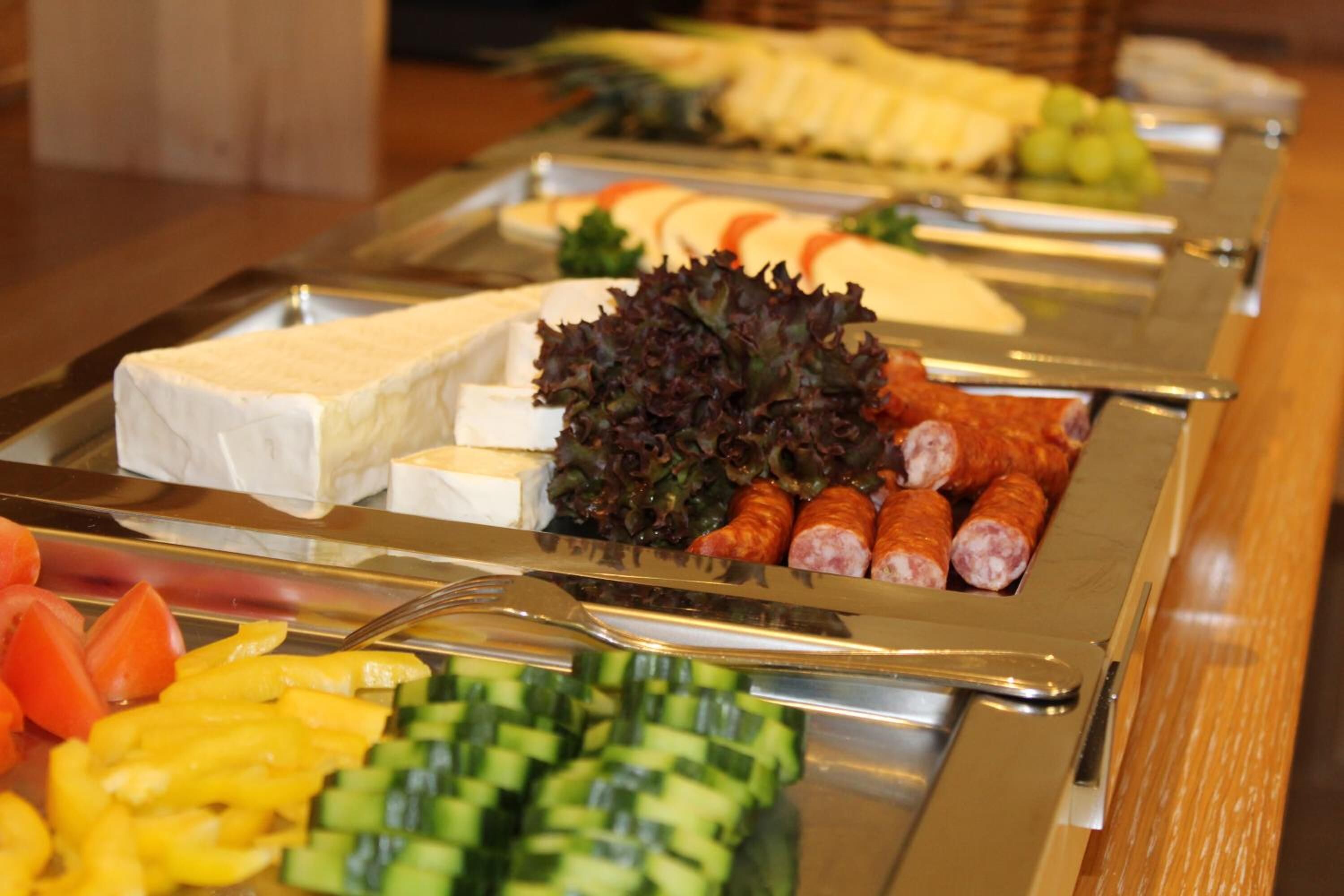 Un bufé con diversos alimentos, entre ellos queso, embutidos y verduras.