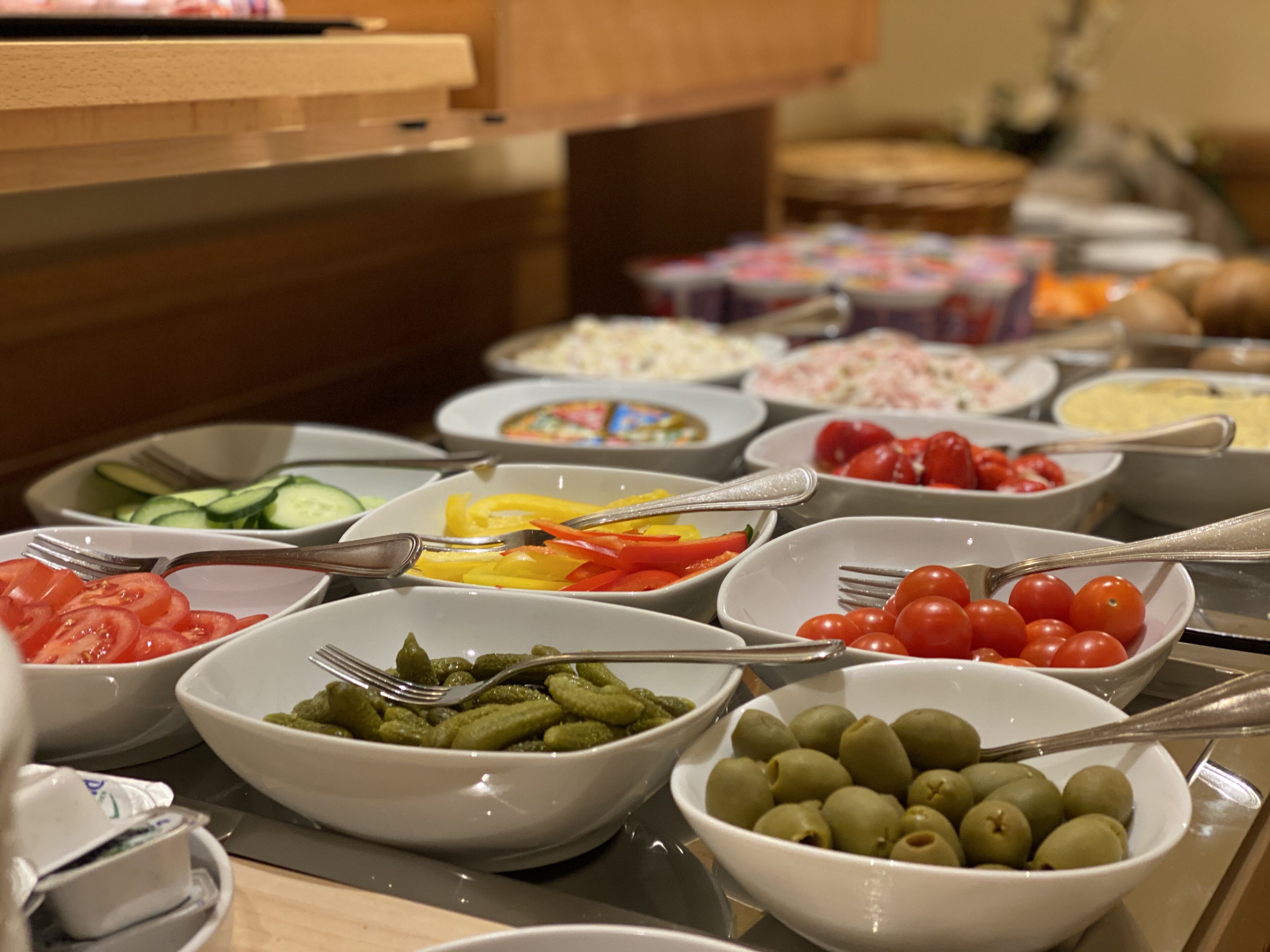 Un bufé con diversos alimentos, entre ellos verduras, aceitunas y tomates.