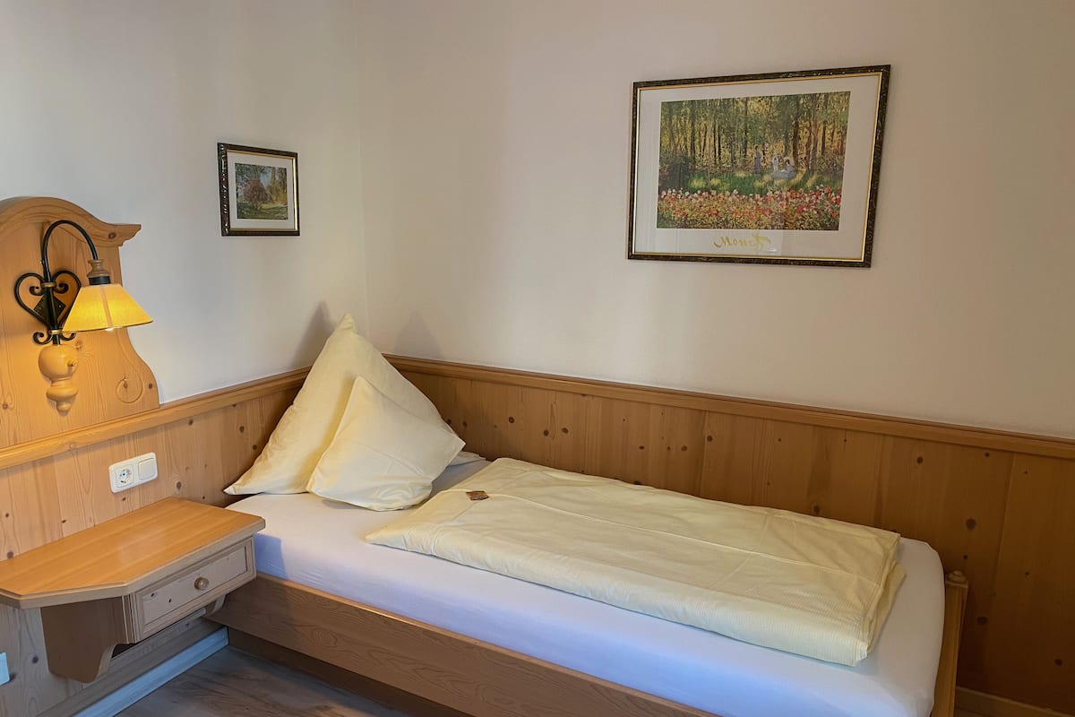 A single bed with a wooden headboard, a bedside table with a lamp, and two framed pictures on the wall.