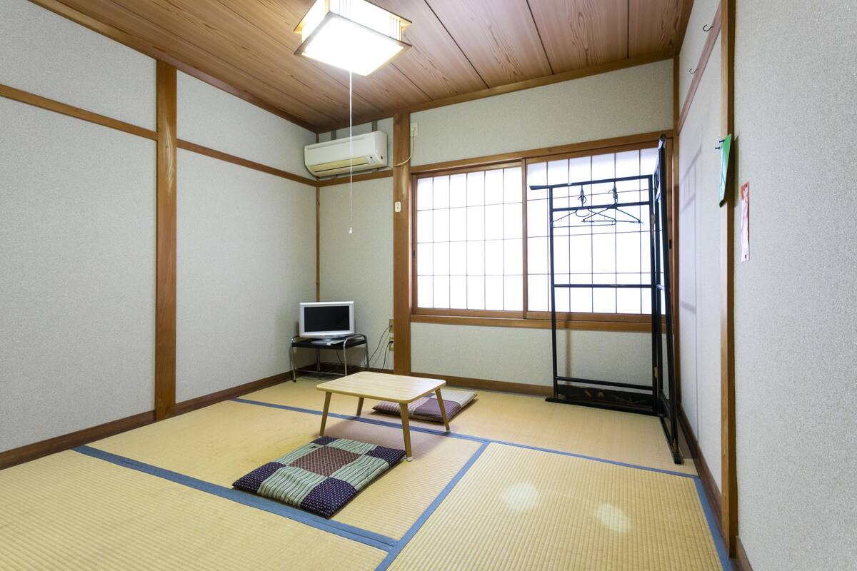 Um quarto japonês tradicional com tatames, uma mesa baixa, uma televisão e uma porta de correr.