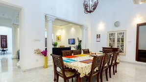 Un coin repas avec une table dressée pour six personnes, entourée de chaises en bois. Un lustre est suspendu au-dessus de la table, et on aperçoit un téléviseur à l’arrière-plan.