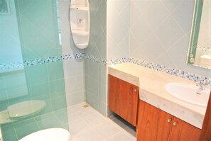 A bathroom with a glass shower enclosure, a white toilet, a wooden vanity with a sink, and a mirror.