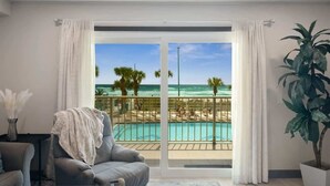 Une chambre avec vue sur une piscine et une plage, un fauteuil gris et une plante en pot.
