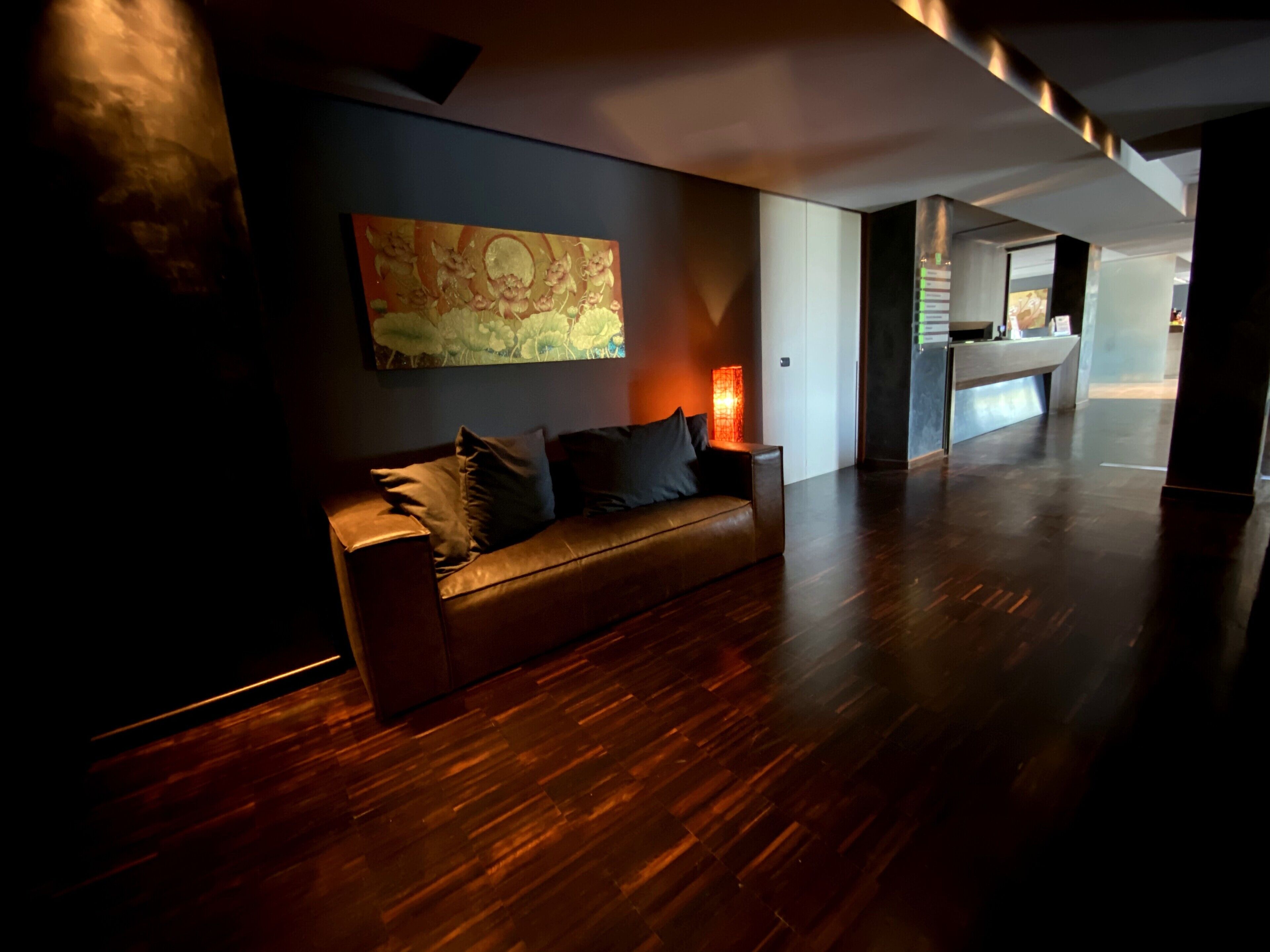 Un hall d’entrée moderne avec un parquet en bois foncé, un canapé en cuir agrémenté de coussins, un grand tableau abstrait et un lampadaire.