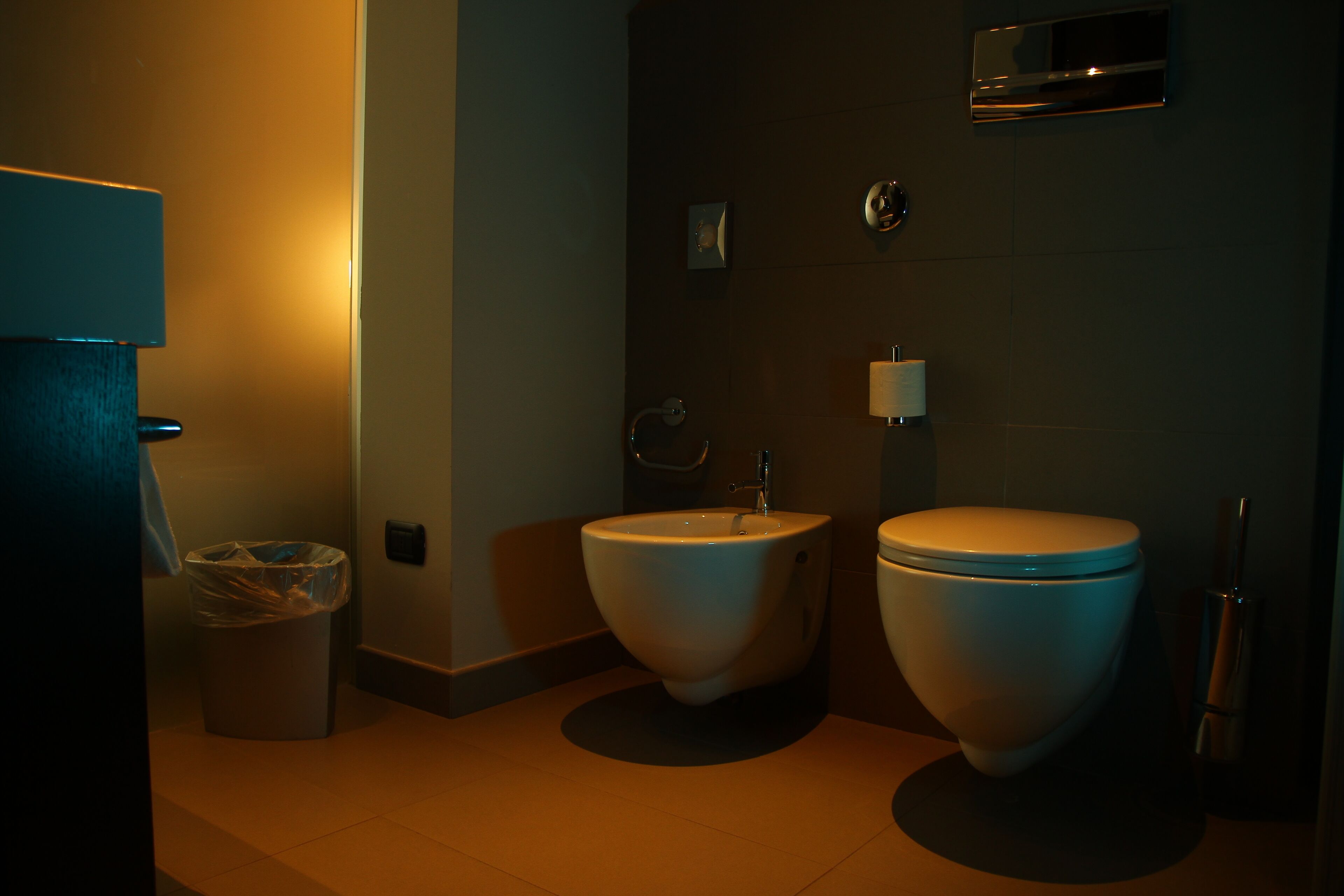 A bathroom with a bidet, toilet, and trash can.