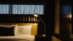 Una habitación de hotel con una cama, una mesita de noche, una lámpara y una ventana con cortinas.